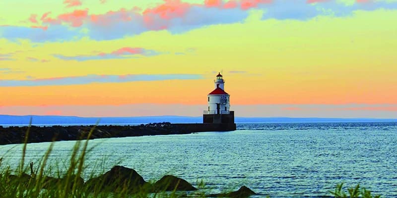 White lighthouse with red roof on a pier under a vibrant yellow and orange sunset sky.