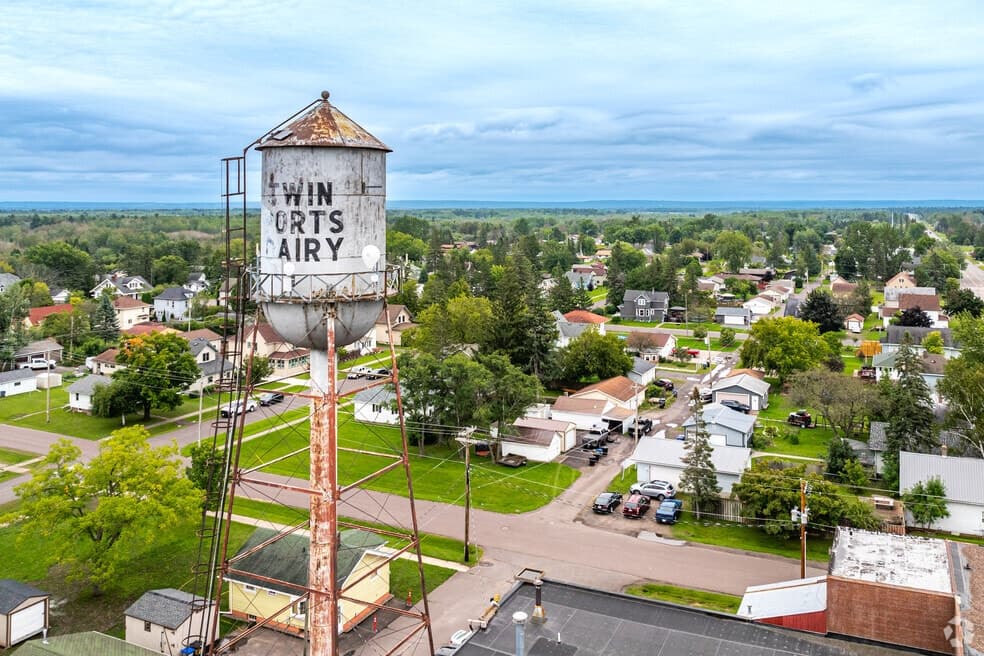 Rusty Twin Ports Dairy water tower stands tall over a small town neighborhood and trees.