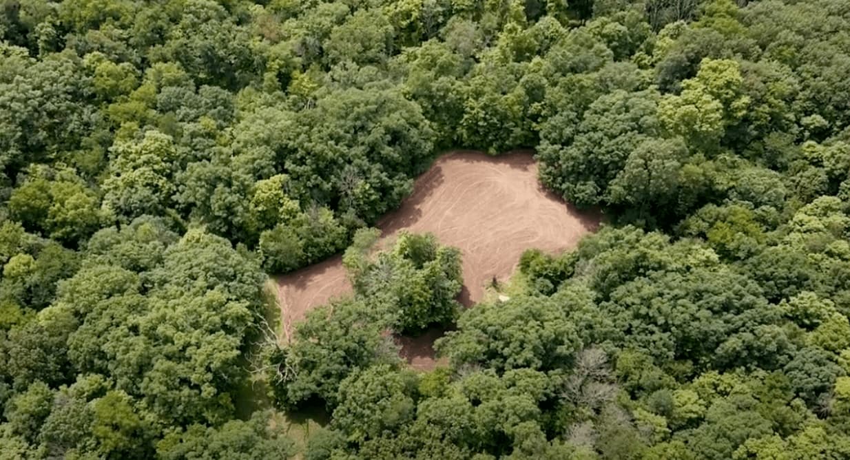 Aerial view of a brown dirt clearing surrounded by a dense, lush green forest.